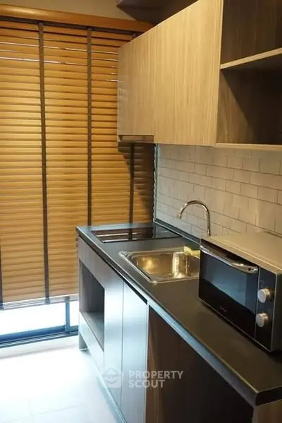 Modern kitchen with sleek cabinets and microwave, featuring wooden blinds and a compact sink area.