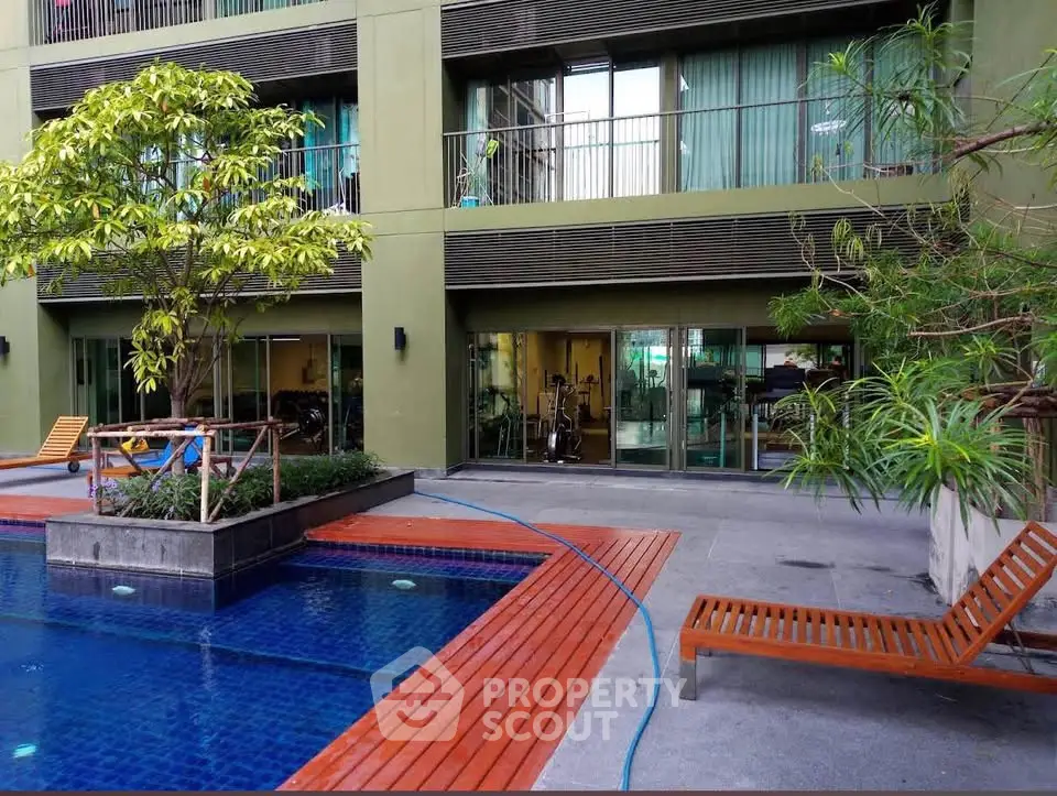 Modern apartment building with pool and gym access, featuring lush greenery and stylish outdoor seating.
