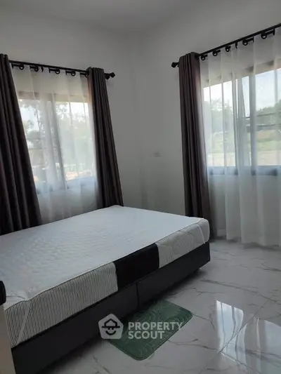 Bright bedroom with large windows and modern decor, featuring a comfortable bed and elegant curtains.