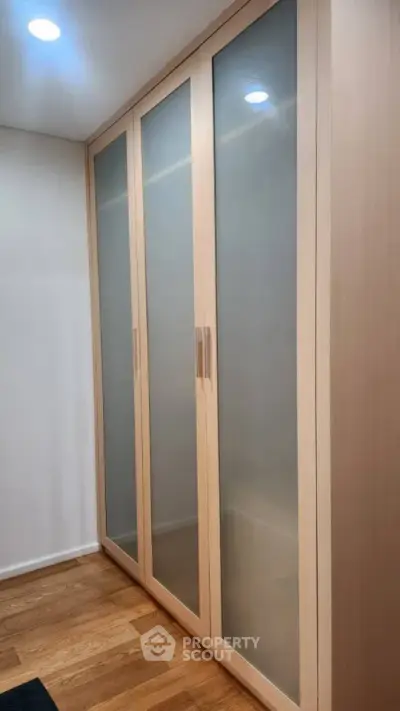Spacious walk-in closet with frosted glass doors and wooden flooring.