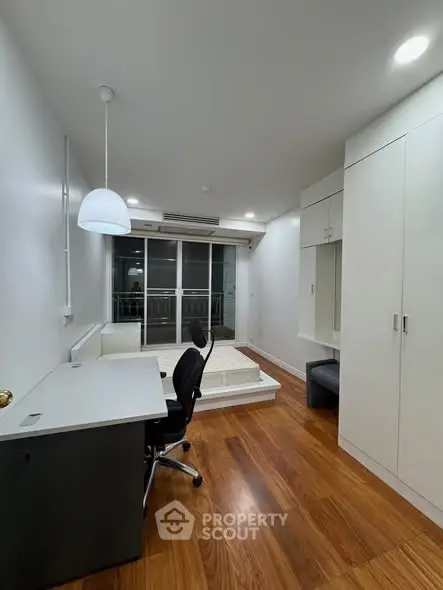 Modern study room with sleek desk, chair, and built-in storage, featuring hardwood floors and balcony access.