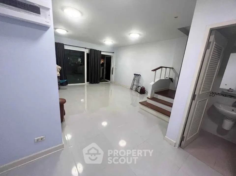 Spacious living room with modern lighting and staircase, ideal for family gatherings.