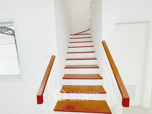 Modern minimalist staircase with wooden steps and white walls in a bright interior space.