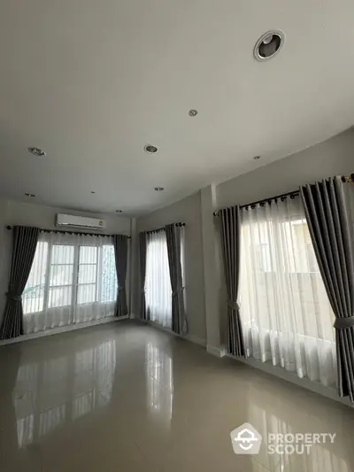 Spacious unfurnished living room with large windows and elegant curtains