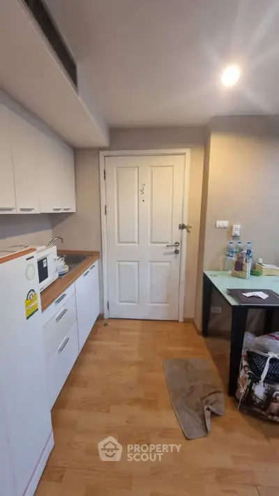 Compact kitchen area with white cabinets and wooden flooring in cozy apartment