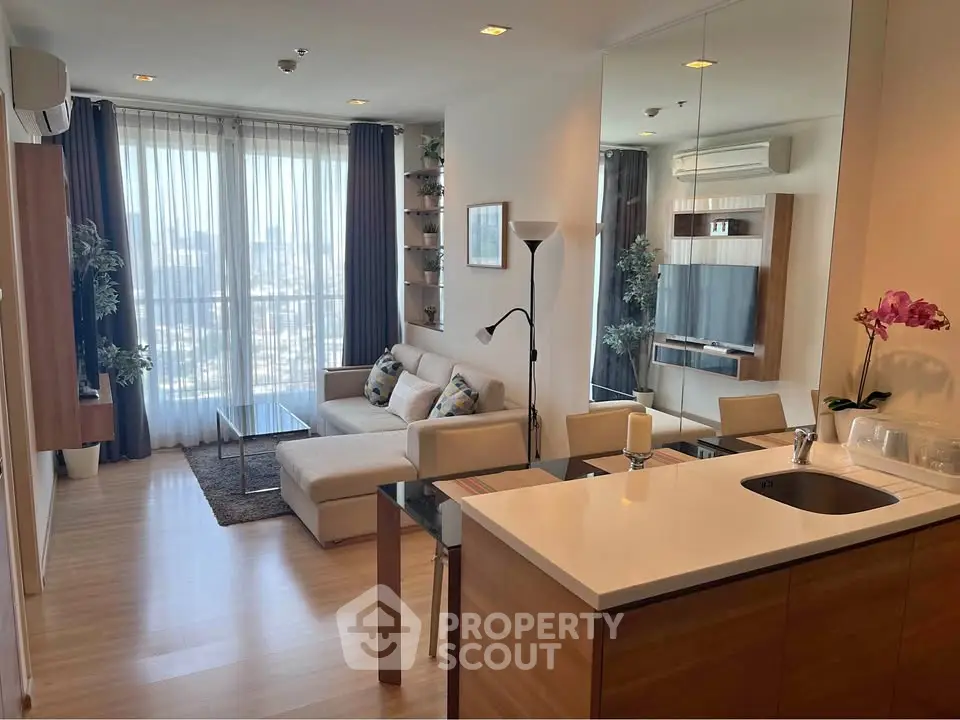 Modern living room with open kitchen, featuring stylish decor and large windows with city view.