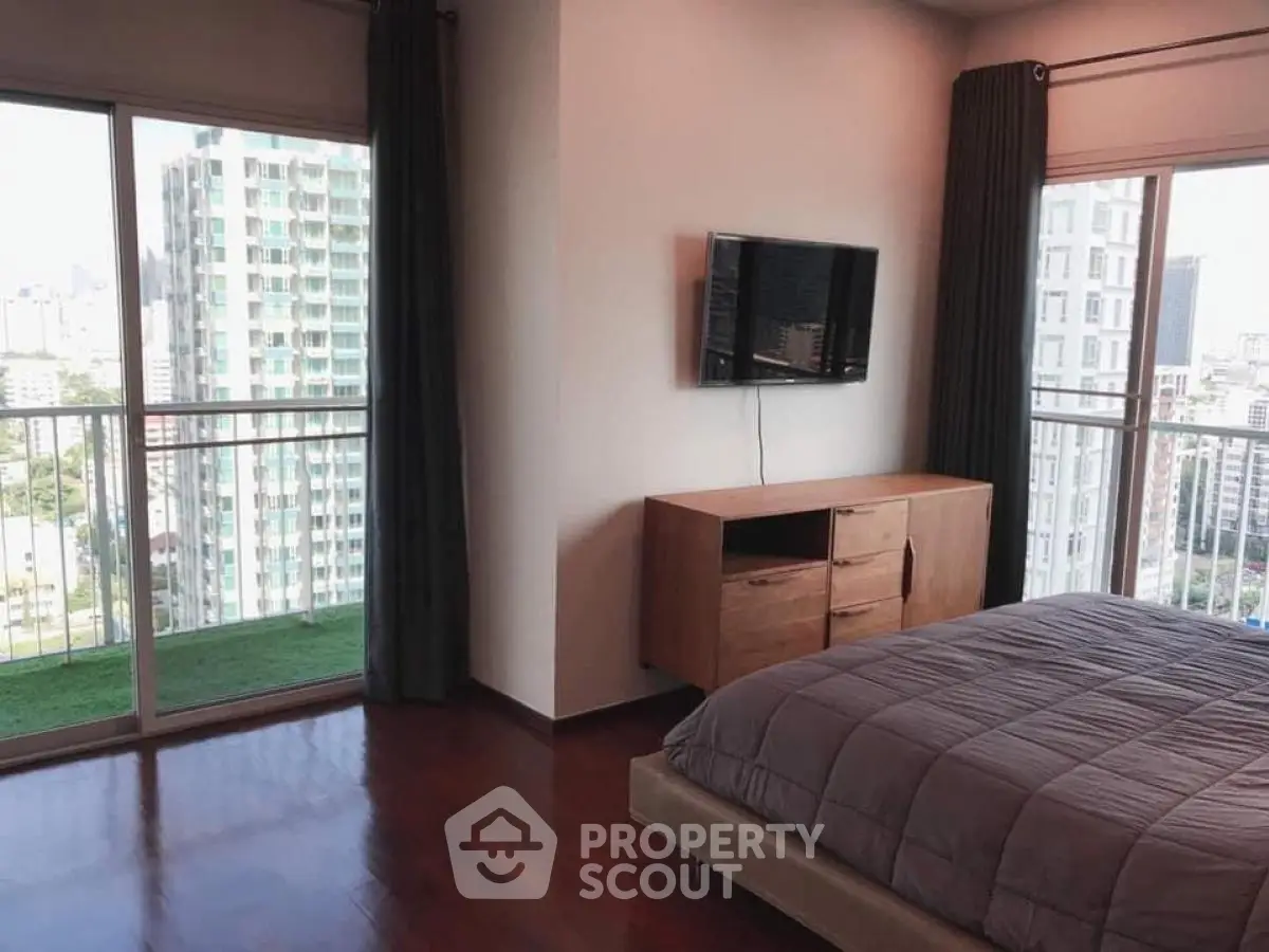 Spacious bedroom with large windows offering stunning city views and modern furnishings.