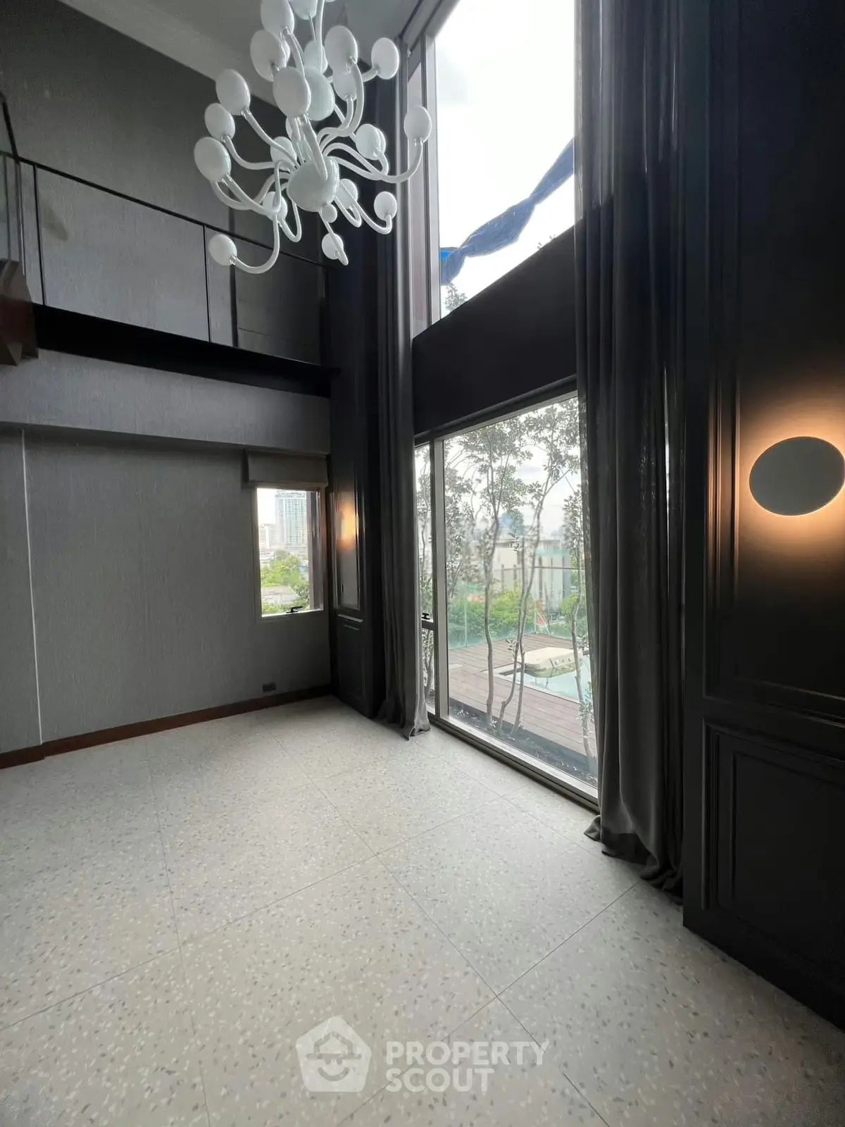 Luxurious high-ceiling living room with large windows and elegant chandelier in modern apartment.