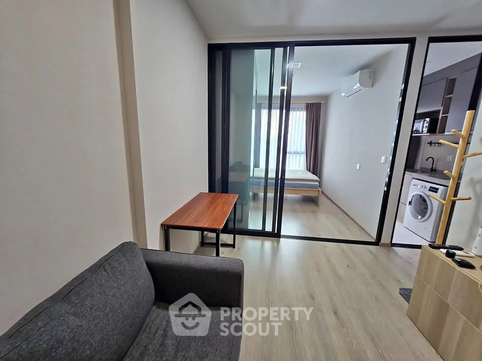 Modern apartment interior with glass partition, cozy living area, and bedroom view.