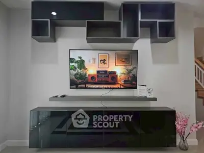 Modern living room with sleek black entertainment unit and wall-mounted TV, stylish shelving, and decorative plants.