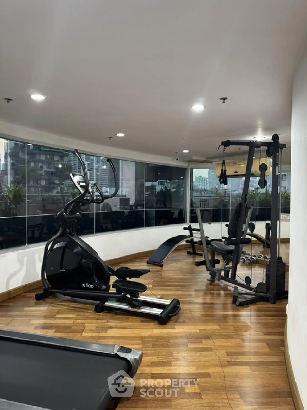 Modern gym with city view, featuring state-of-the-art exercise equipment and wooden flooring.