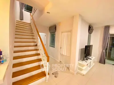 Modern living room with staircase and TV, featuring elegant curtains and bright lighting.