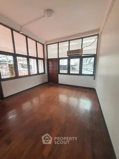 Spacious room with wooden flooring and large windows, perfect for natural light.