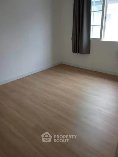 Spacious empty room with wooden flooring and large window, perfect for customization.