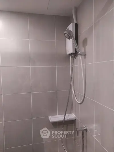 Modern bathroom with sleek tiled walls and a mounted shower unit, perfect for a contemporary home.