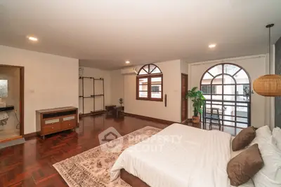 Spacious bedroom with wooden flooring and large windows in a modern home.