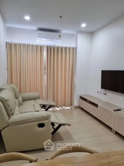 Spacious and modern living room with plush reclining sofa, sleek entertainment unit, and warm lighting, perfect for relaxation and hosting.