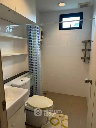Modern bathroom with white tiles, compact design, and natural light from window.