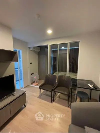 Modern living room with sleek furniture and open layout, featuring a TV and dining area.