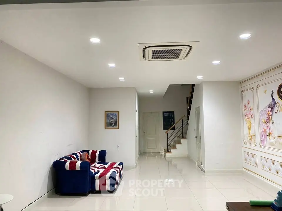 Spacious living room with modern decor and stylish sofa, featuring bright lighting and a sleek staircase.