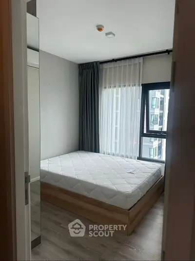 Modern bedroom with large window and minimalist decor in urban apartment.