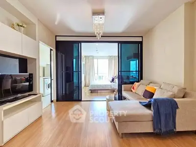 Modern living room with sliding glass doors leading to a bright bedroom, featuring cozy sofa and TV unit.
