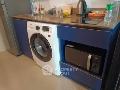 Modern kitchen with washing machine, microwave, and sleek blue cabinetry.