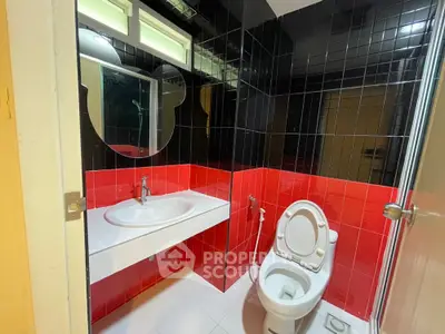 Modern bathroom with striking red and black tiles, featuring a sleek sink and toilet.