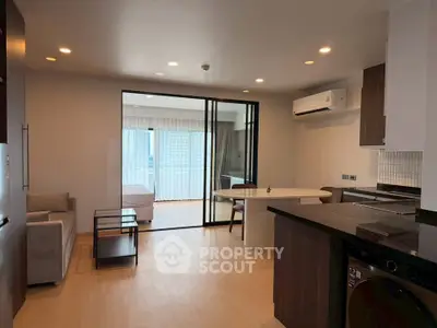 Modern open-plan living room with kitchen and bedroom view, featuring sleek furniture and ample natural light.