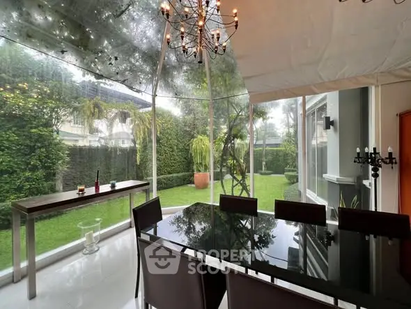 Luxurious dining area with glass walls offering a stunning garden view, elegant chandelier, and sleek furniture.