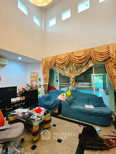 Spacious living room with high ceiling and elegant curtains, featuring cozy sofas and modern decor.