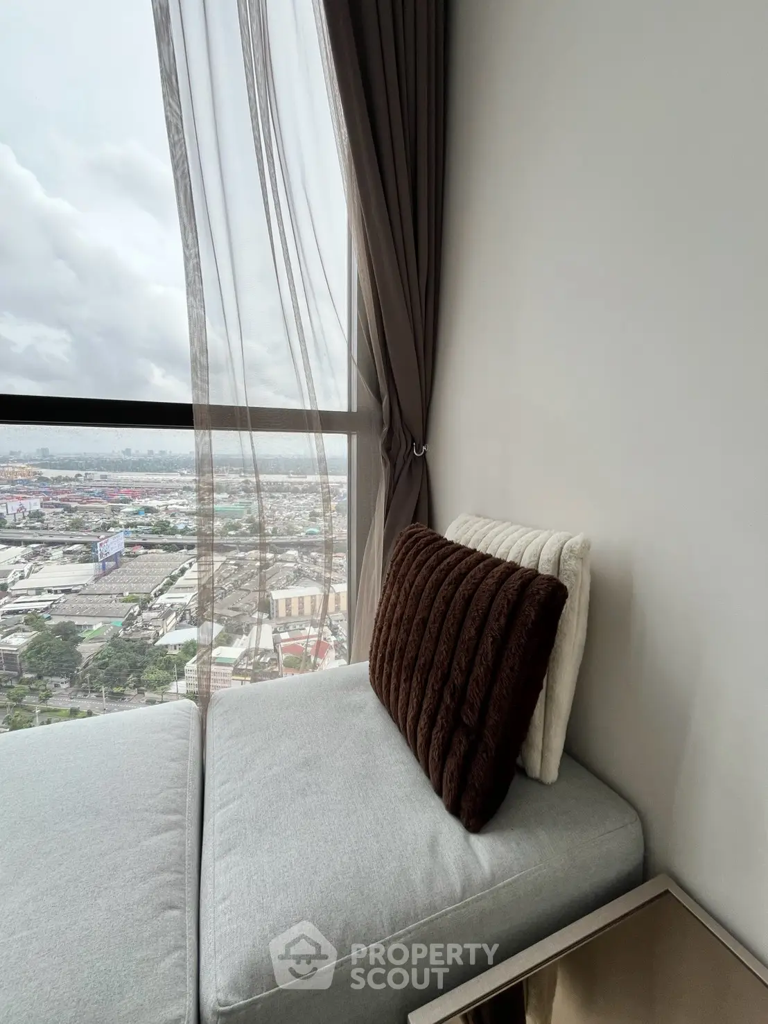 Cozy corner unit with stunning city view from large window, featuring elegant curtains and plush seating.