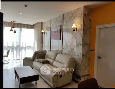 Elegant living room with marble accent wall, plush beige sofa, and large windows offering abundant natural light.