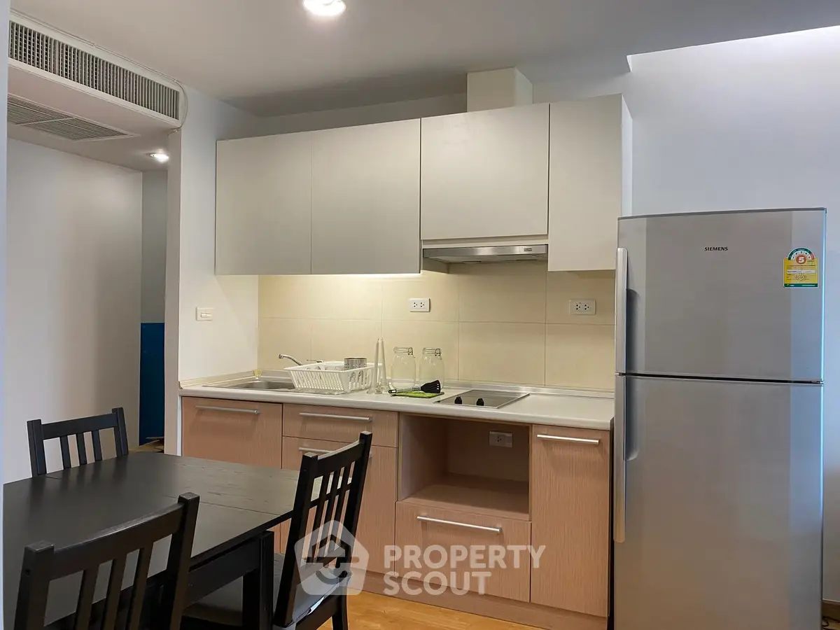 Modern kitchen with sleek cabinetry and stainless steel fridge in a cozy apartment setting.