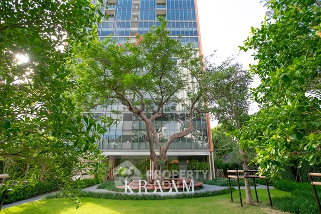 Modern high-rise building with lush green garden and trees in front, offering serene urban living.