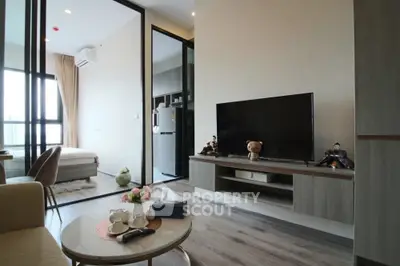 Modern living room with TV, cozy seating, and bedroom view in stylish apartment.