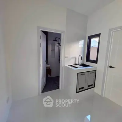 Modern minimalist kitchen with sleek cabinetry and adjacent bathroom entrance.