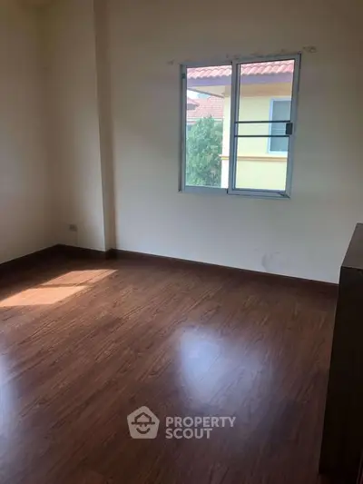 Spacious empty room with wooden flooring and a window offering natural light.