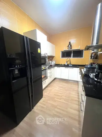Modern kitchen with sleek black appliances and wooden flooring, featuring a spacious layout and contemporary design.