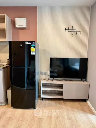 Modern living room with sleek black fridge and flat-screen TV, showcasing stylish interior design.