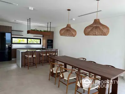 Modern open-layout kitchen and dining area with stylish wooden furniture and pendant lighting.