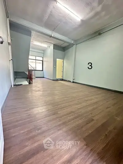 Spacious room with wooden flooring and high ceiling, ideal for versatile use.