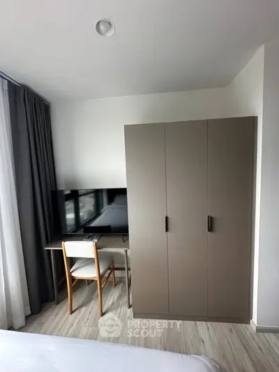 Modern bedroom with wardrobe, desk, and TV, featuring sleek design and natural light.