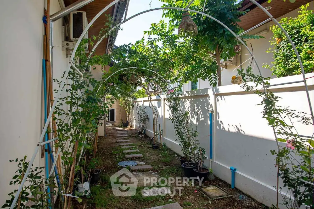 Charming garden pathway with lush greenery and arch trellis in a serene residential setting.