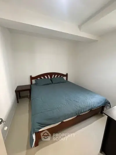 Cozy bedroom with wooden bed frame and teal bedding in a minimalist design.