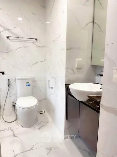 Modern bathroom with sleek design and marble tiles, featuring a stylish sink and toilet.