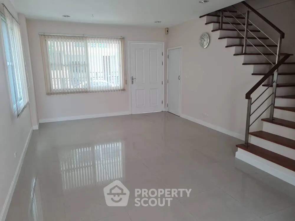 Spacious empty living room with staircase and large window, perfect for customization.