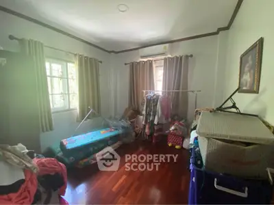 Cozy bedroom with wooden flooring and ample natural light, featuring a window and air conditioning unit.