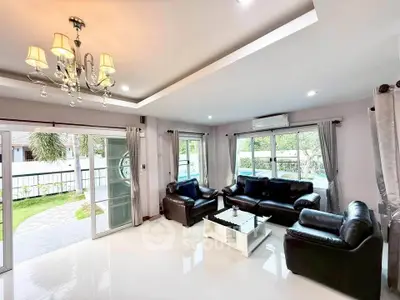 Spacious living room with elegant chandelier and garden view, featuring modern leather sofas and large windows.