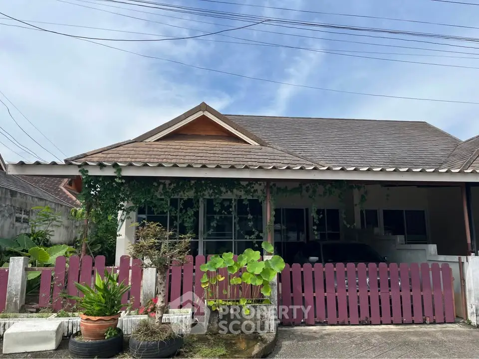 Charming single-story house with a rustic wooden fence and lush greenery, perfect for serene living.